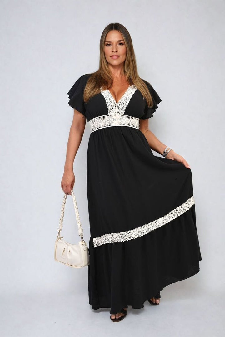 Woman in Alejandra V-neck Lace Trim Maxi Dress holding a white purse, showcasing elegant style and sophistication.