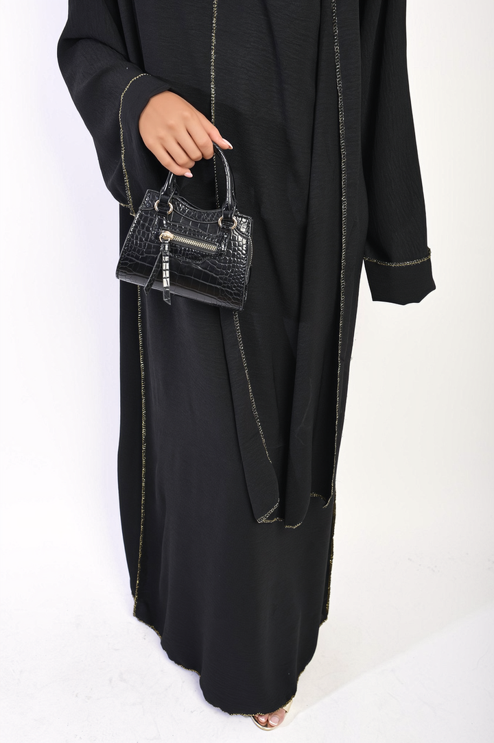 Person holding a black purse next to the Long Sleeve Closed Abaya Maxi Dress with Embellished Piping, showcasing elegant design details.