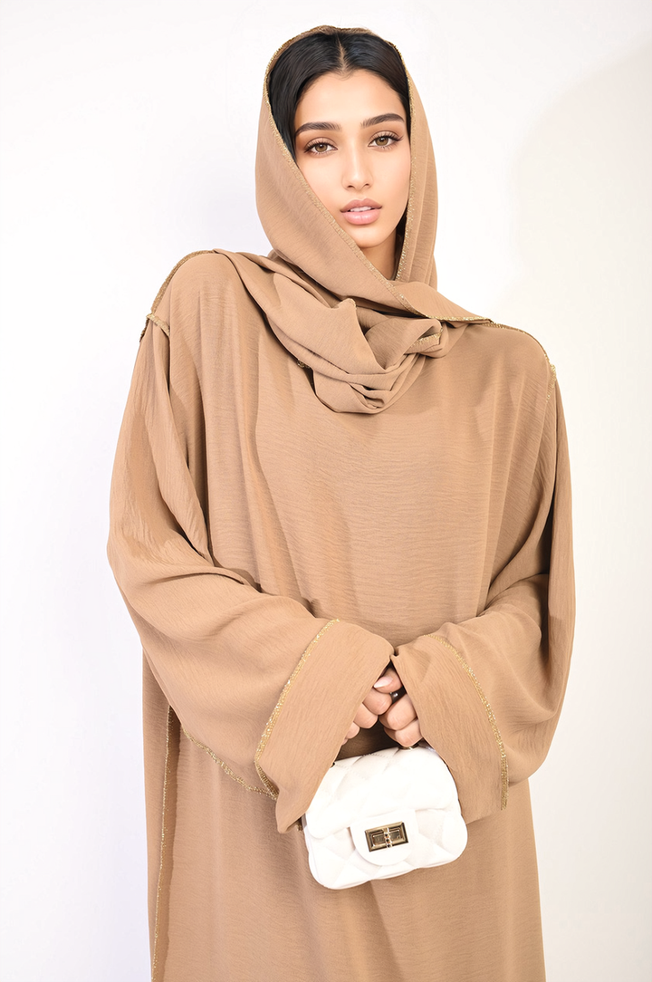 Woman in brown robe holding a white purse, showcasing the Long Sleeve Closed Abaya Maxi Dress With Embellished Piping, highlighting its modest style and elegant design.