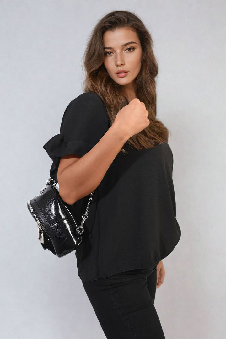 Woman holding a black handbag, wearing the Alexandra Frill Sleeve Top, showcasing its elegant frill sleeves perfect for versatile, stylish holiday and everyday outfits.