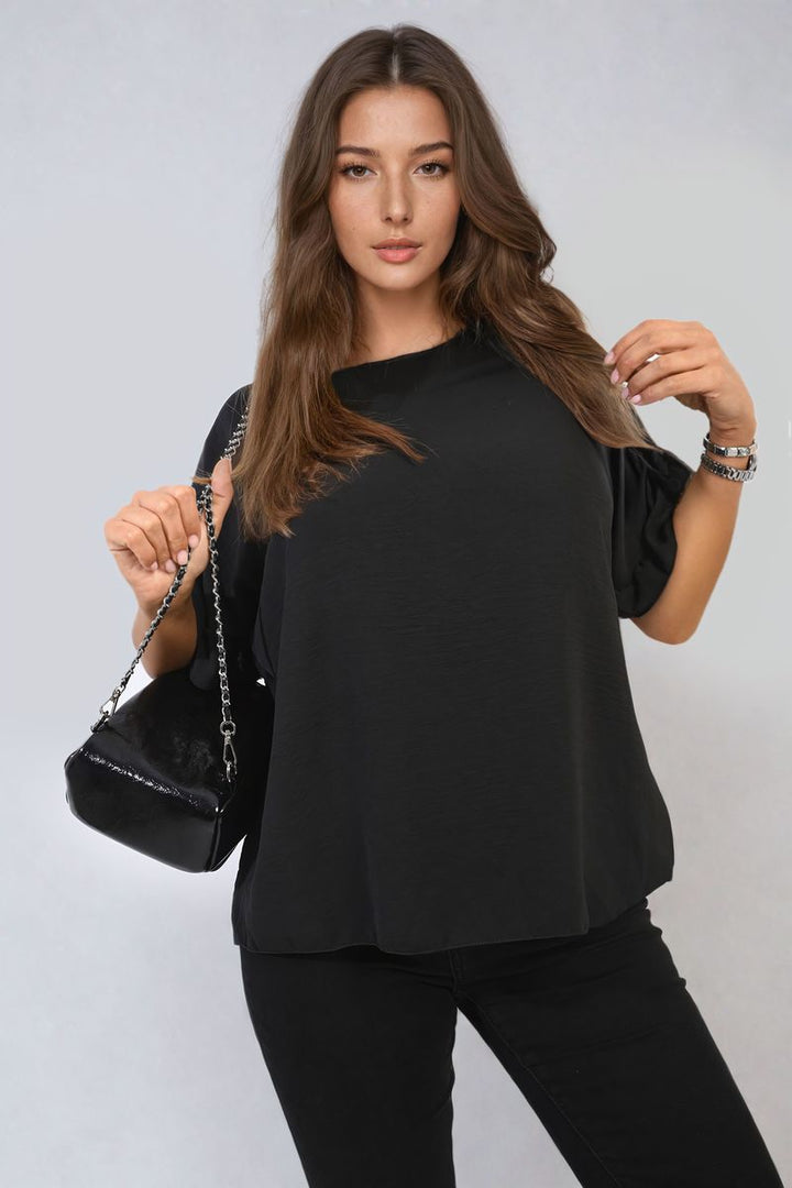 Woman wearing the Alexandra Frill Sleeve Top holds a black purse, showcasing the top's elegance and playful charm in a stylish, everyday fashion look.