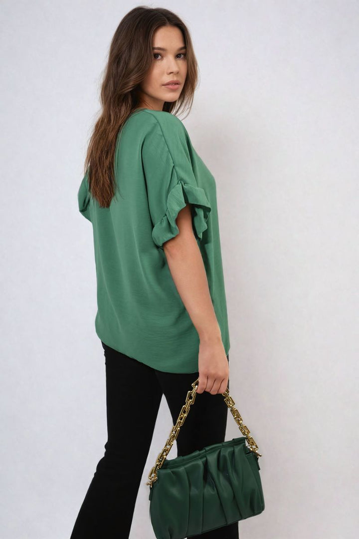 Woman in green Alexandra Frill Sleeve Top holding a green purse with gold chain, highlighting the top's elegant frill sleeves and stylish design.