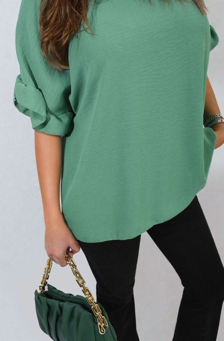 Woman elegantly holding a green purse with a gold chain, wearing the Alexandra Frill Sleeve Top, showcasing its stylish design and playful frill sleeves.