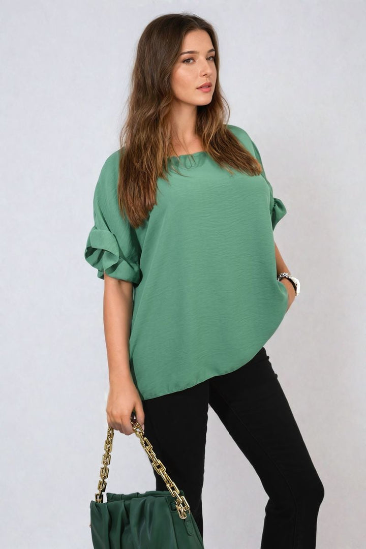 Woman wearing Alexandra Frill Sleeve Top, holding a green purse, showcasing the top's elegant, playful design and versatile style.