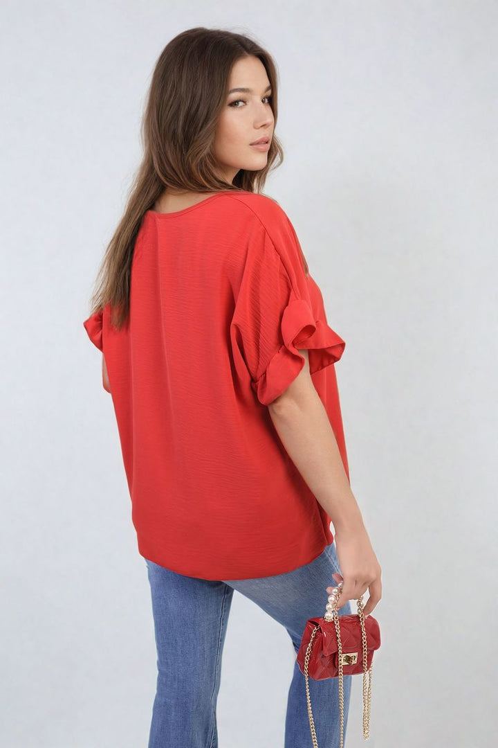 Woman wearing the Alexandra Frill Sleeve Top, paired with jeans, holding a red purse. The top showcases elegant frill sleeves for a stylish, versatile look.