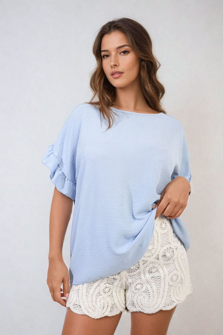 Woman wearing Alexandra Frill Sleeve Top with white shorts, showcasing its elegant and playful design, ideal for stylish holiday and everyday wear.