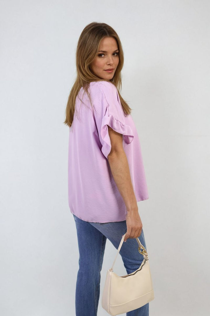 Woman wearing Alexandra Frill Sleeve Top, holding a handbag; the top showcases elegance and playful charm, perfect for versatile holiday and everyday style.