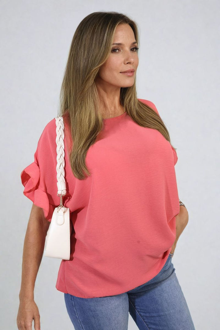 A woman wearing the Alexandra Frill Sleeve Top, showcasing its elegant frill sleeves and comfortable fit, paired casually with jeans.