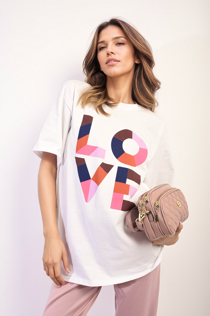 Woman holding the Amanda Oversized Love Slogan Print Top, showcasing its relaxed fit and bold slogan, suitable for casual outings.