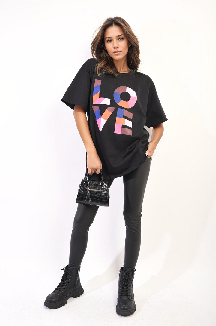 Woman wearing the Amanda Oversized Love Slogan Print Top, holding a black purse, paired with black boots, showcasing a casual, relaxed style.