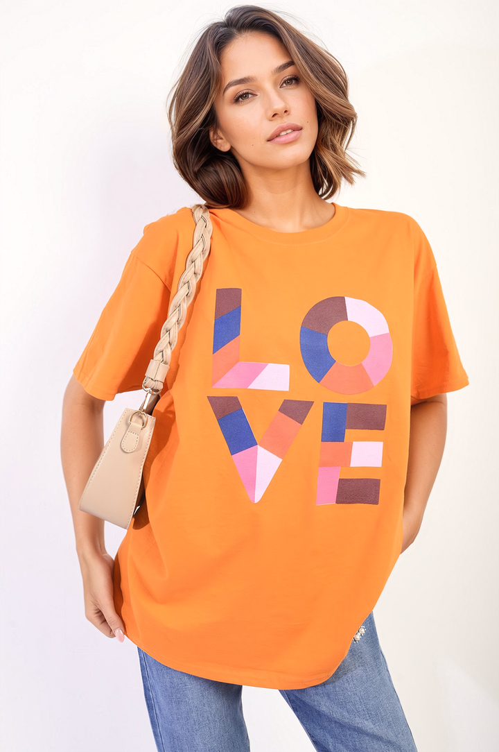 Woman wearing the Amanda Oversized Love Slogan Print Top with purse, showcasing its relaxed fit and positive slogan, ideal for casual outings.