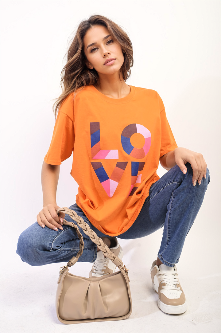 Woman modeling the Amanda Oversized Love Slogan Print Top, showcasing its relaxed fit and stylish design, paired with jeans and accessories.