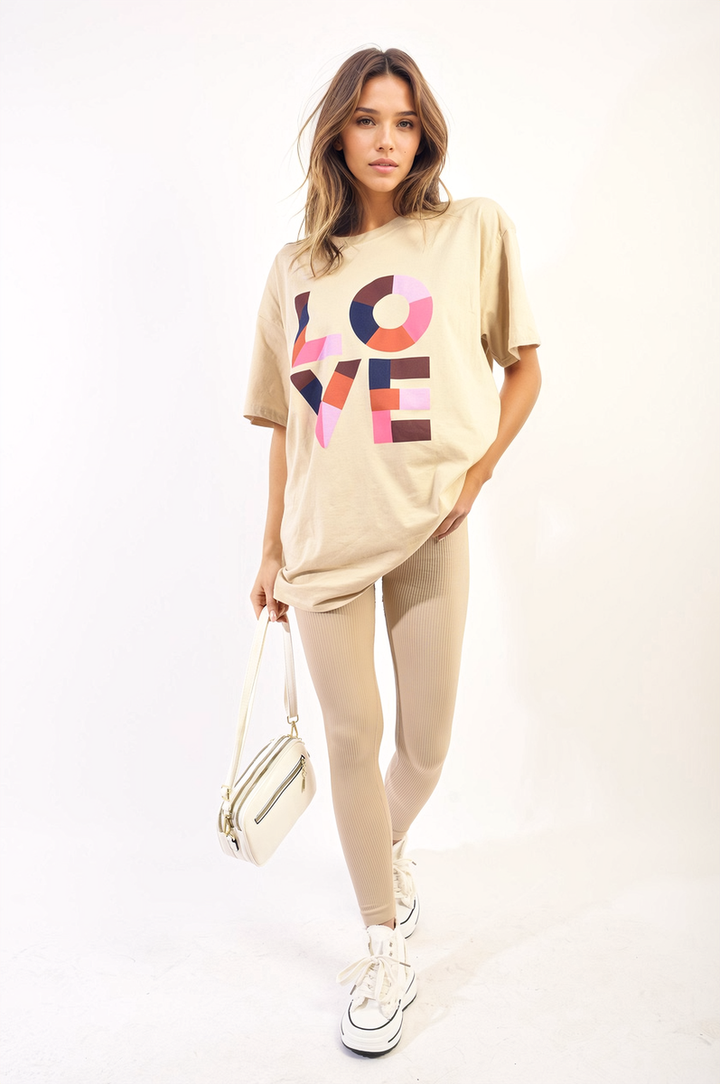 Woman wearing an oversized top with Love slogan, holding a white bag, showcasing the Amanda Oversized Love Slogan Print Top from Holiday Clothes UK.