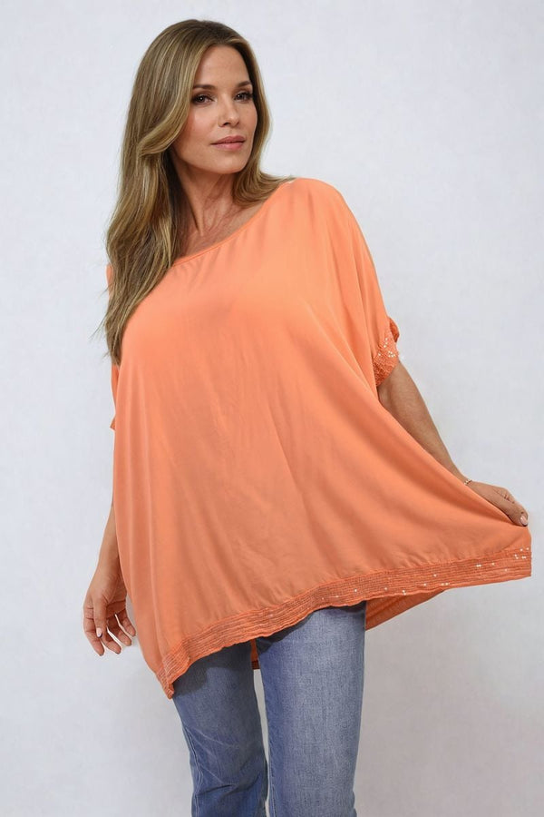 Woman wearing an Amber Oversized Sequin Hem Flare Sleeve Top, showcasing its relaxed fit, dramatic sleeves, and shimmering sequin hem detail.