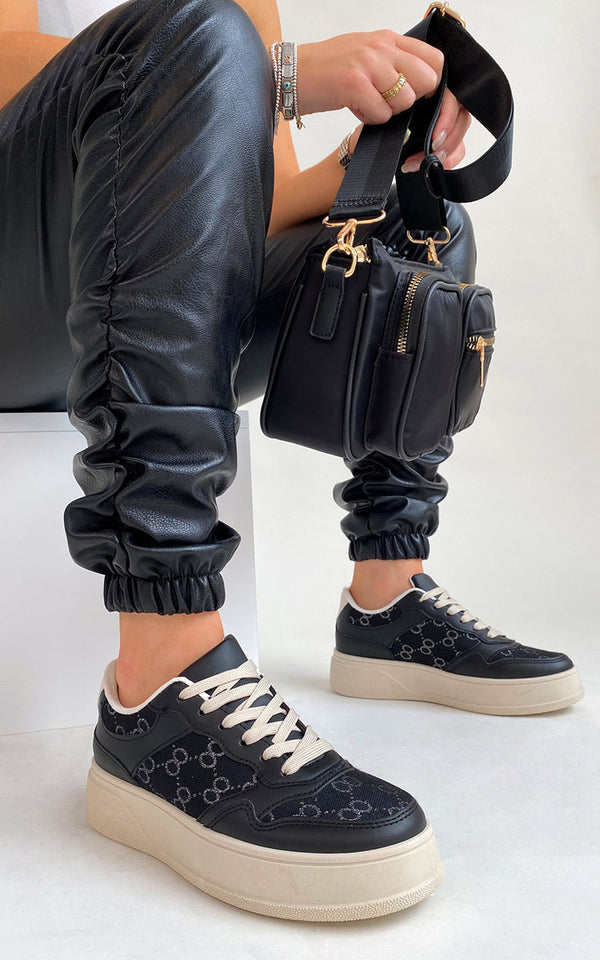 Person wearing black pants, holding a black purse, showcasing Annie Printed trainers with a stylish all-over print design, ideal for everyday wear and fashion-forward looks.