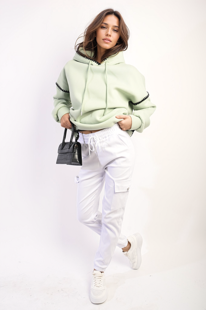 Woman in green hoodie, white pants, showcasing Janelle Drawstring Waist Cargo Joggers with elasticated cuffs and cargo pockets, emphasizing comfort and style.