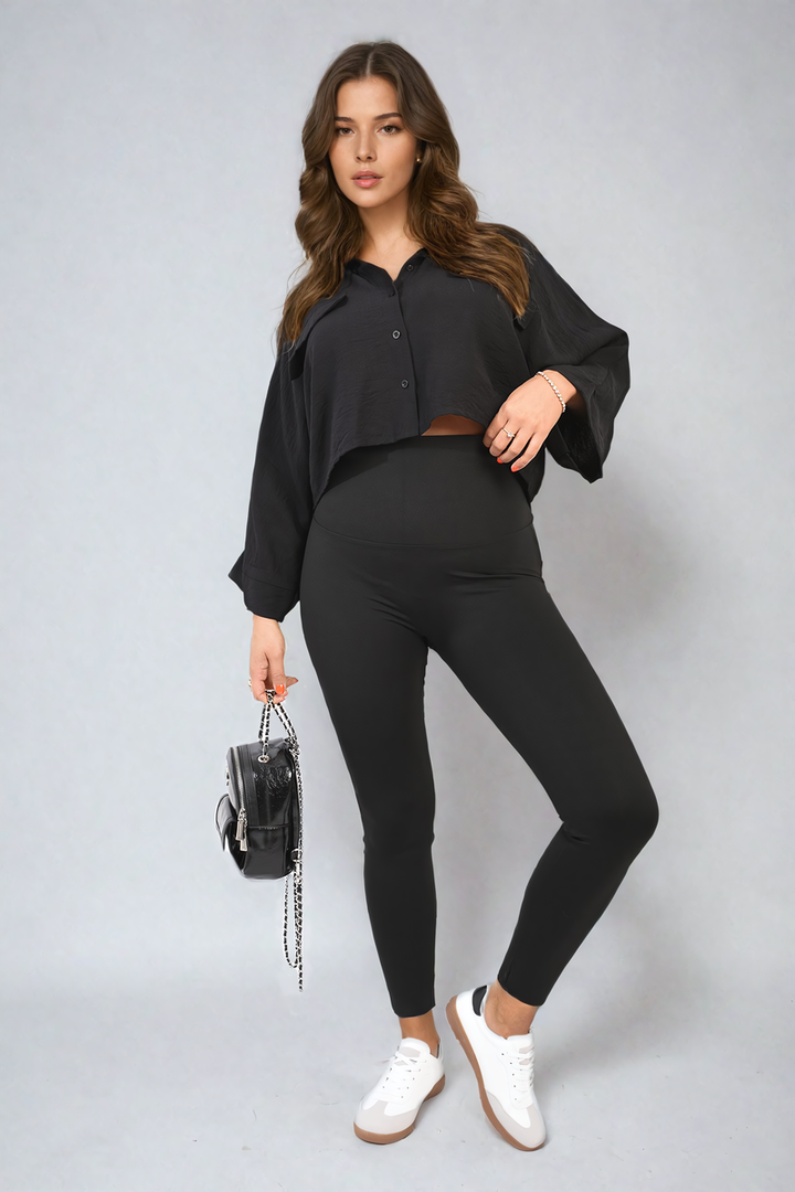 Woman in black outfit showcasing Camila High Waist Wide Waistband Leggings, holding a purse, highlighting their stylish and versatile design for activewear enthusiasts.