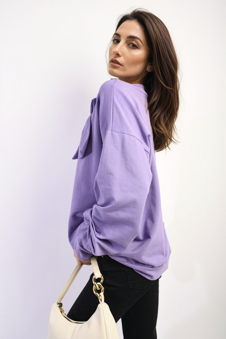 Woman in a purple long sleeve bow detail jumper holding a white purse, showcasing a stylish and cozy fashion piece from Holiday Clothes UK.