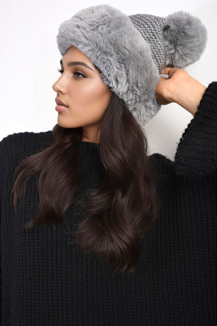 Woman wearing the Carly Faux Fur Knitted Winter Hat with a pom-pom, showcasing its stylish design and plush texture for winter warmth.