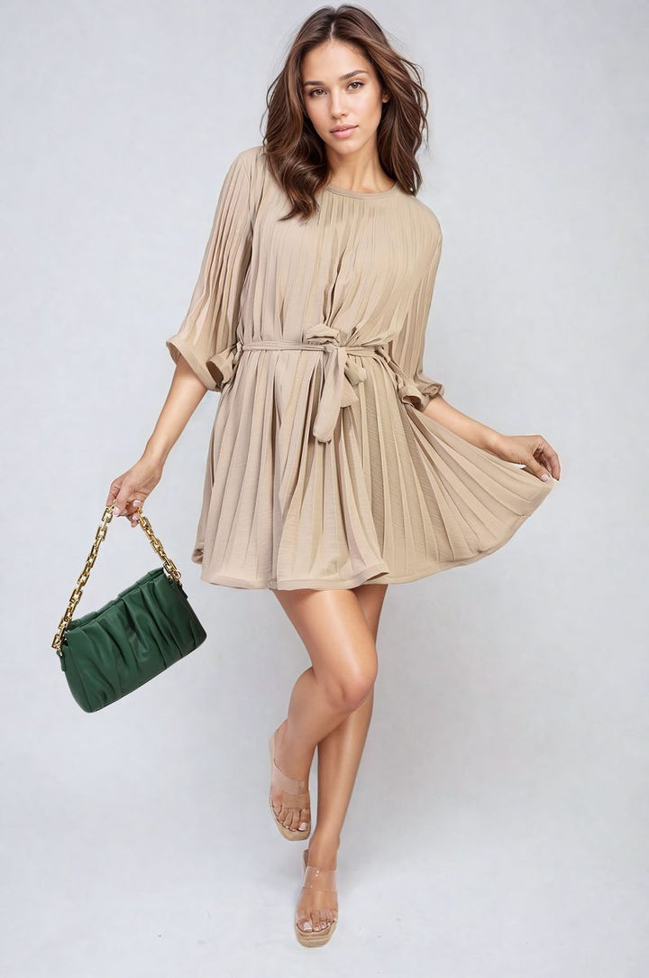 Woman holding a Pleated Tie Waist Mini Dress, featuring exquisite pleating and a tie waist design, perfect for elevating your wardrobe with chic elegance.