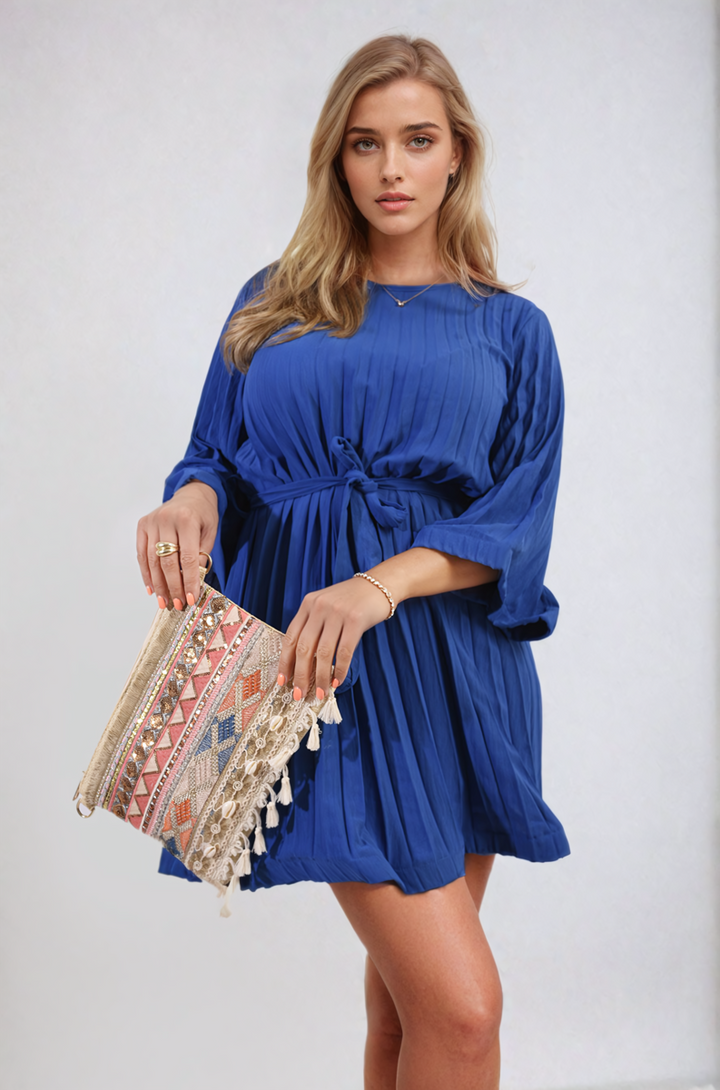 Woman in a Pleated Tie Waist Mini Dress holding a purse, showcasing its elegant design with pleating and tie waist detail.