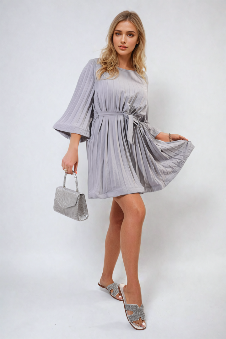 Pleated Tie Waist Mini Dress on a woman, featuring elegant pleats and a flattering tie waist, paired with a silver purse and high heels.