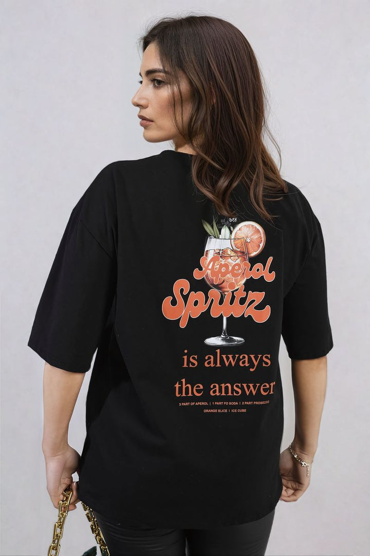 Woman wearing Aperol Spritz Cocktail Graphic Top, ideal for summer hangouts and beach days, holding a chain with a drink nearby.