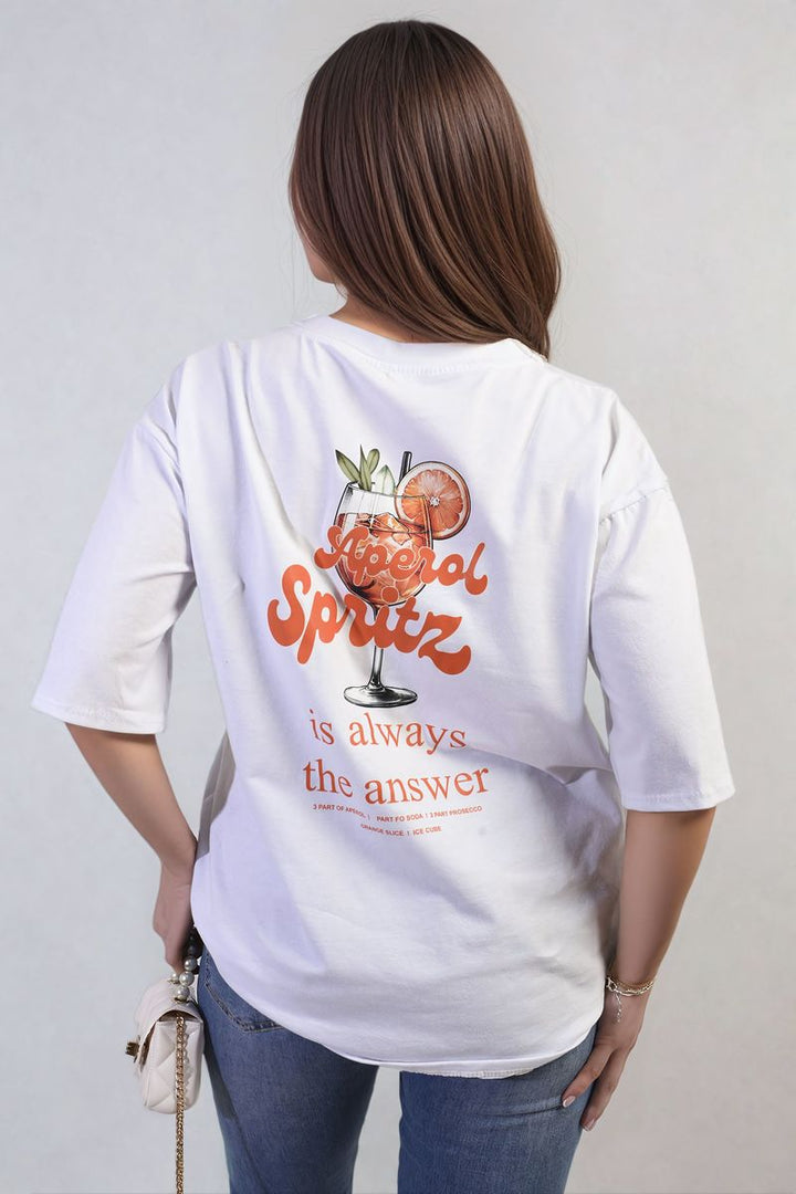 Woman wearing Aperol Spritz Cocktail Graphic Top with vibrant design, paired with blue jeans, emphasizing casual style. Perfect for summer hangouts or beach days.