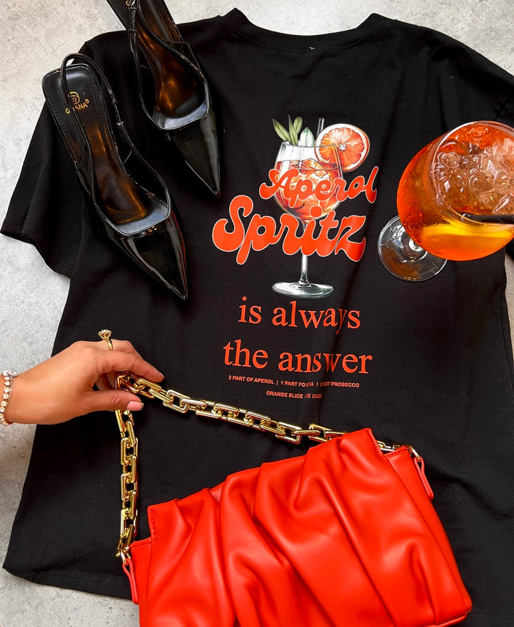 Aperol Spritz Cocktail Graphic Top held alongside a purse and shoes, perfect for casual outings and summer vibes.