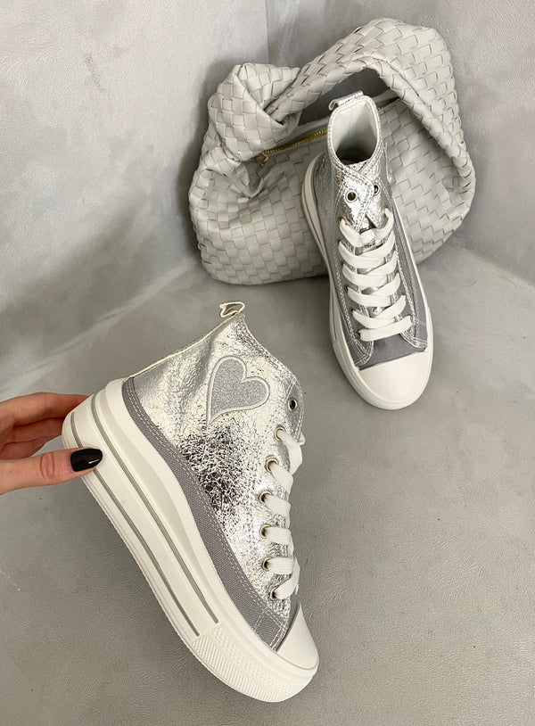 High Top Lace Up Heart Detailed Kids Trainers featuring a silver finish, white laces, and heart accents, held by a person, ideal for trendy children's wear.