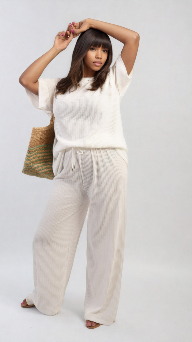 Woman in white ribbed oversized top and drawstring wide-leg trousers holds a straw bag, showcasing the cozy co-ord set from Holiday Clothes UK.