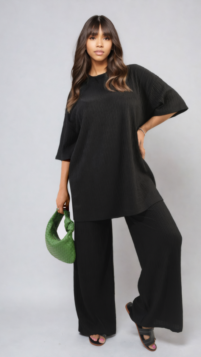 Woman in black outfit wearing the Daniela Ribbed Oversized Top and Drawstring Wide Leg Trouser Co-ord Set, holding a green purse.