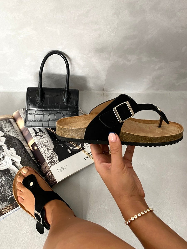 Hand holding a black T-strap Slip On Flat Thong Sandal next to a purse, highlighting its minimalist design and casual comfort.