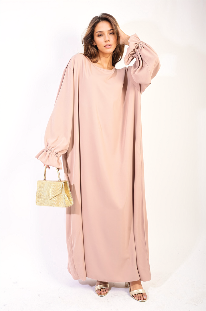 A woman in a pink Abaya Maxi Dress with Elastic Sleeve holds a gold purse, showcasing elegant fashion from Holiday Clothes UK.