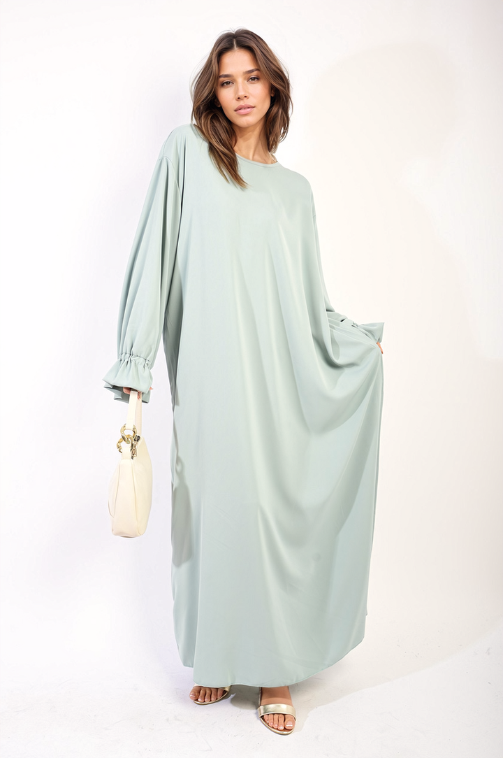 Woman in a long Abaya Maxi Dress with Elastic Sleeves, showcasing a flowing silhouette and gold sandals, embodying elegance and modern style.