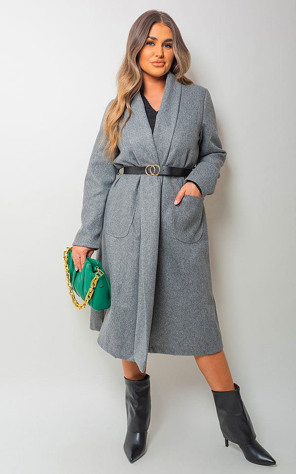 Woman wearing the Delilah Wrap Belted Long Coat, paired with black boots, holding a green purse. The coat's wrap design and belted waist emphasize elegance.