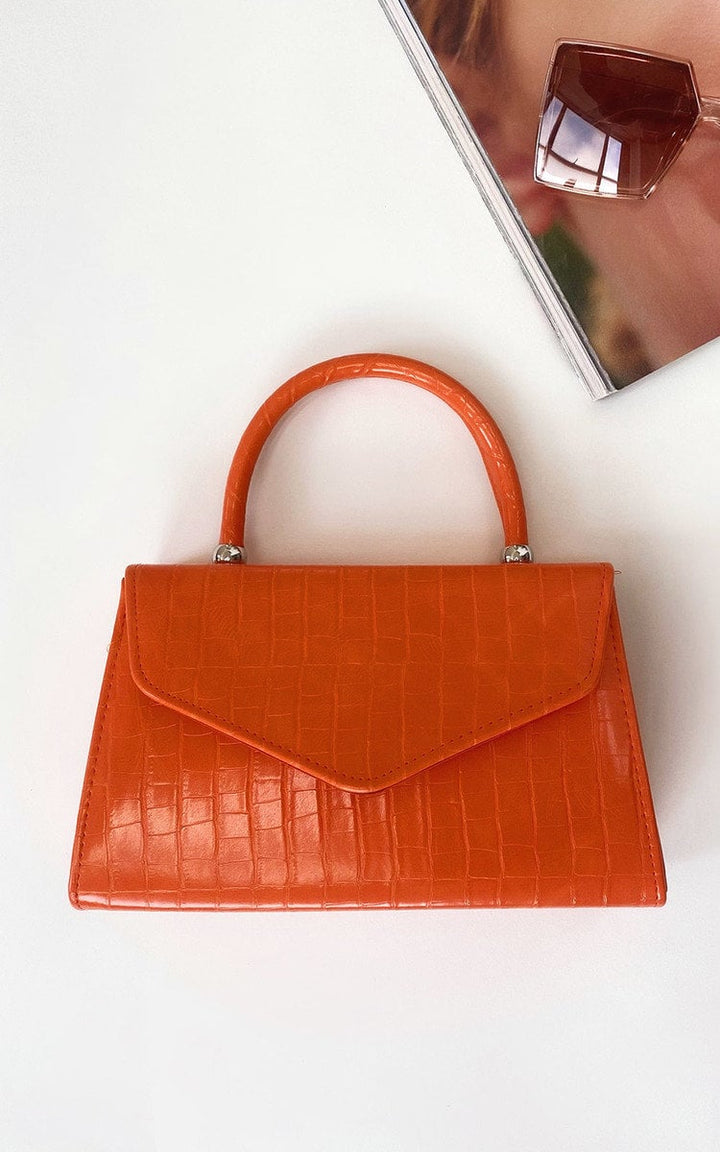 Croc Print Handbag with faux leather, handheld handle, and chain strap displayed on a white surface next to a book and sunglasses.