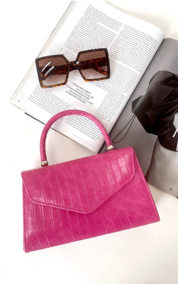 Croc Print Handbag displayed with sunglasses and a book, highlighting its faux leather texture, handheld handle, and chain strap for versatile styling.