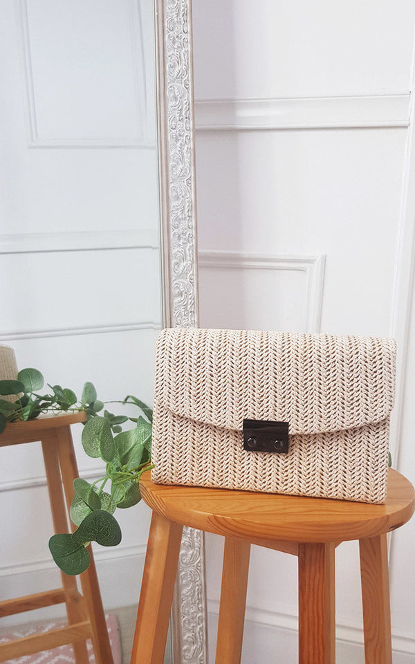 Woven Handbag on a wooden stool, featuring a wicker design with a front clip and long chain strap, perfect for completing any stylish outfit.