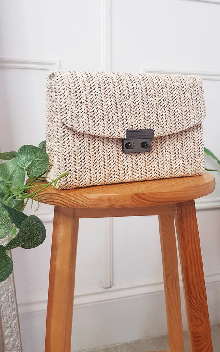 Woven Handbag displayed on a stool, showcasing its wicker material, front clip, and long chain strap, ideal for adding chic style to any outfit.