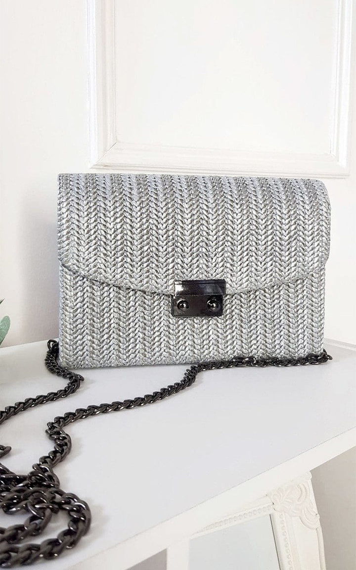 Woven Handbag on a white surface, featuring wicker material with a front clip and long chain strap, ideal for adding chic style to any outfit.