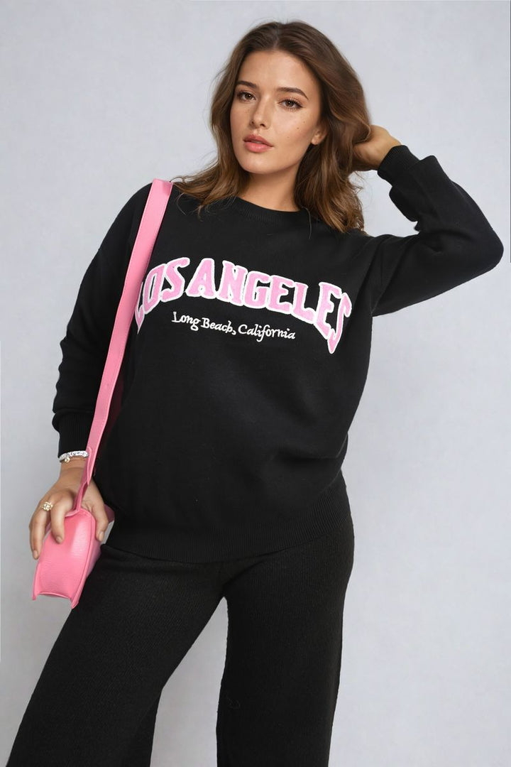 Woman modeling the Los Angeles Graphic Long Sleeve Knitted Jumper, showcasing its cozy knitted fabric and trendy design, suitable for stylish everyday wear.