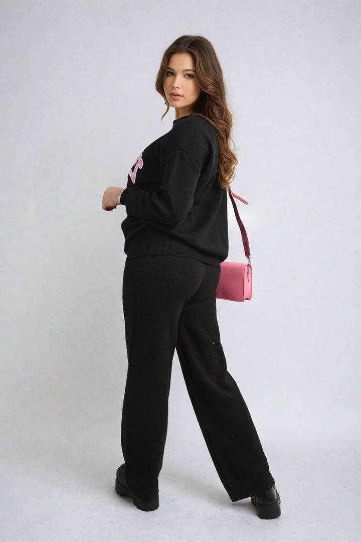 Woman wearing a Los Angeles Graphic Long Sleeve Knitted Jumper, paired with black pants, showcasing a trendy and cozy style perfect for everyday wear.