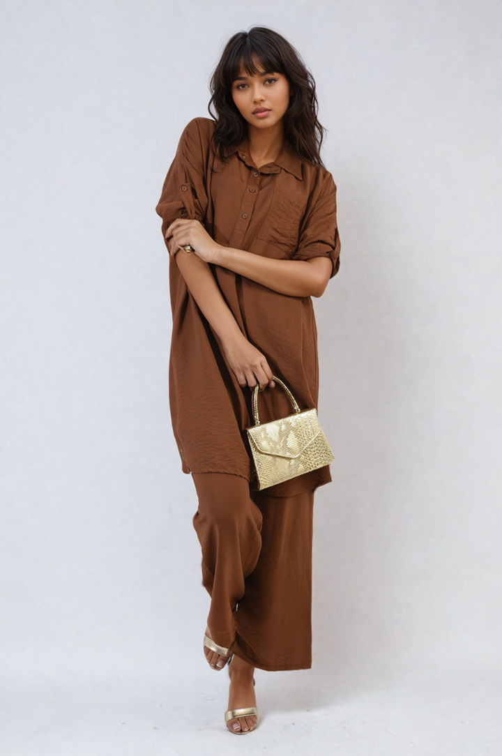 Woman wearing the Dulce Oversized Button Front Shirt & Wide Leg Pants Co-ord Set, holding a gold purse, embodying relaxed, stylish holiday fashion.