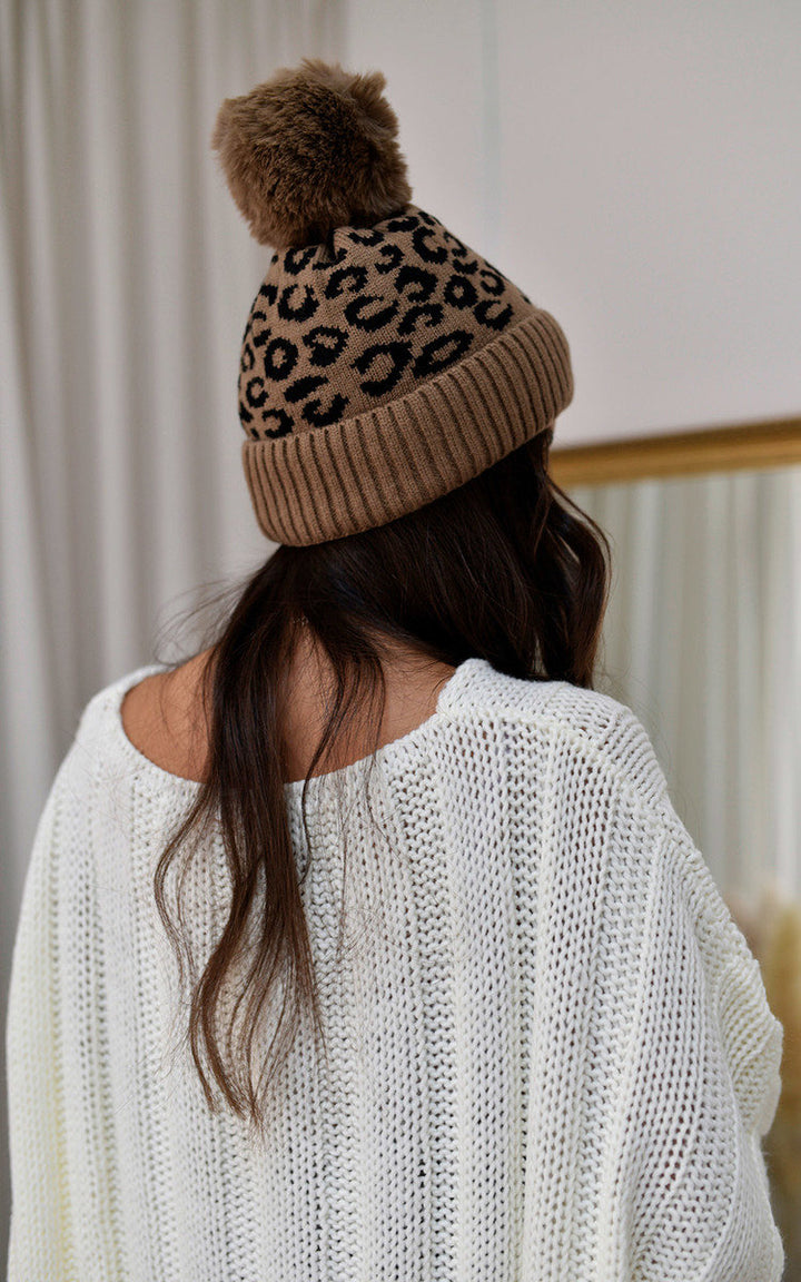 Woman wearing the Edith Faux Fur Lined Beanie Leopard Hat, showcasing its stylish design with a pom-pom detail, perfect for warmth during colder months.