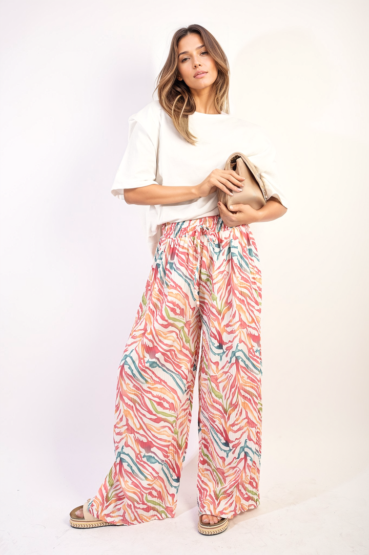 Woman wearing Pleated Wide Leg and Elastic Waist Trousers, holding a purse. The trousers feature a sophisticated pleated design, highlighting style and comfort.