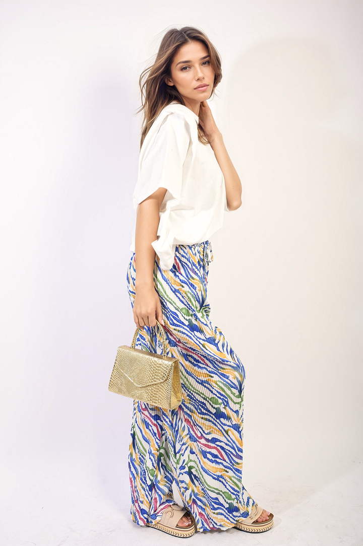 Woman showcasing Pleated Wide Leg and Elastic Waist Trousers, paired with a white shirt and colorful skirt, holding a gold purse.