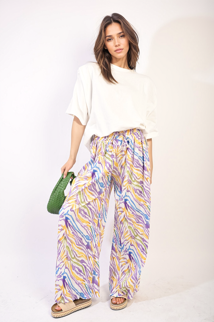 Woman wearing Pleated Wide Leg and Elastic Waist Trousers, holding a green bag. Featuring a sophisticated pleated design and comfortable elastic waistband.