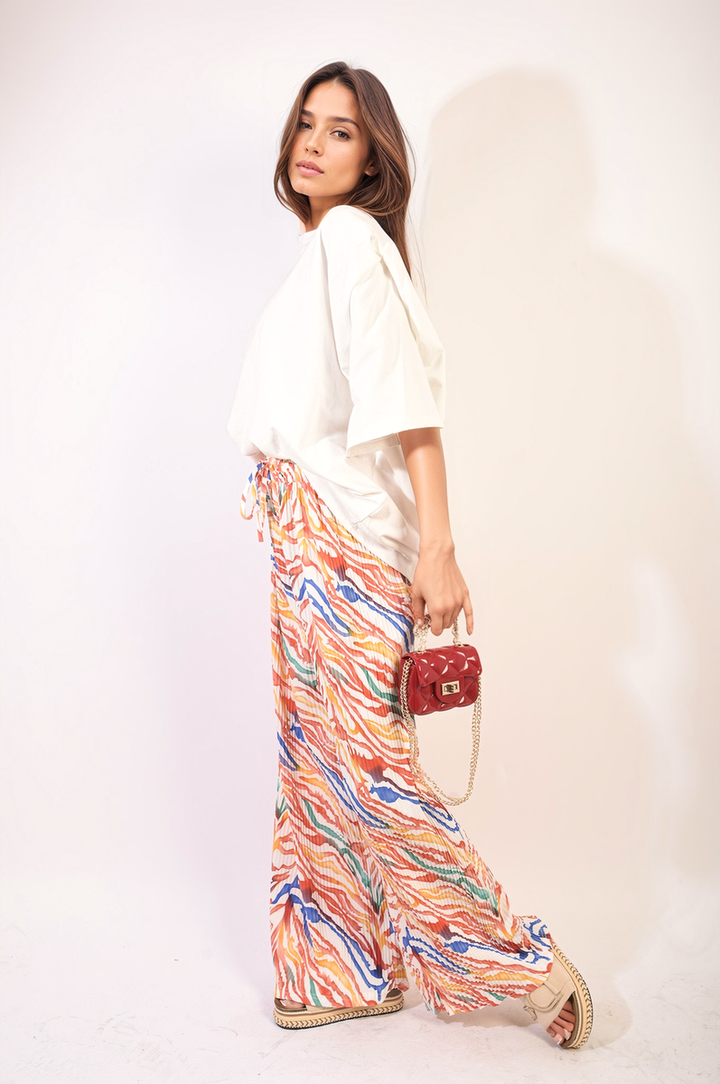 Woman showcasing Pleated Wide Leg and Elastic Waist Trousers, paired with a colorful skirt and red purse, highlighting comfort and style for various occasions.