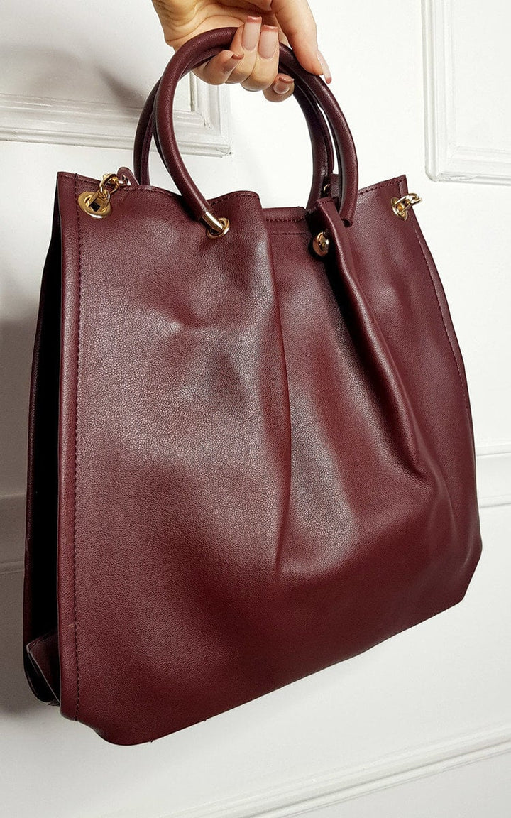 Handbag with faux leather, zip fastening, and detachable shoulder strap, showcased hanging on a door for Holiday Clothes UK.